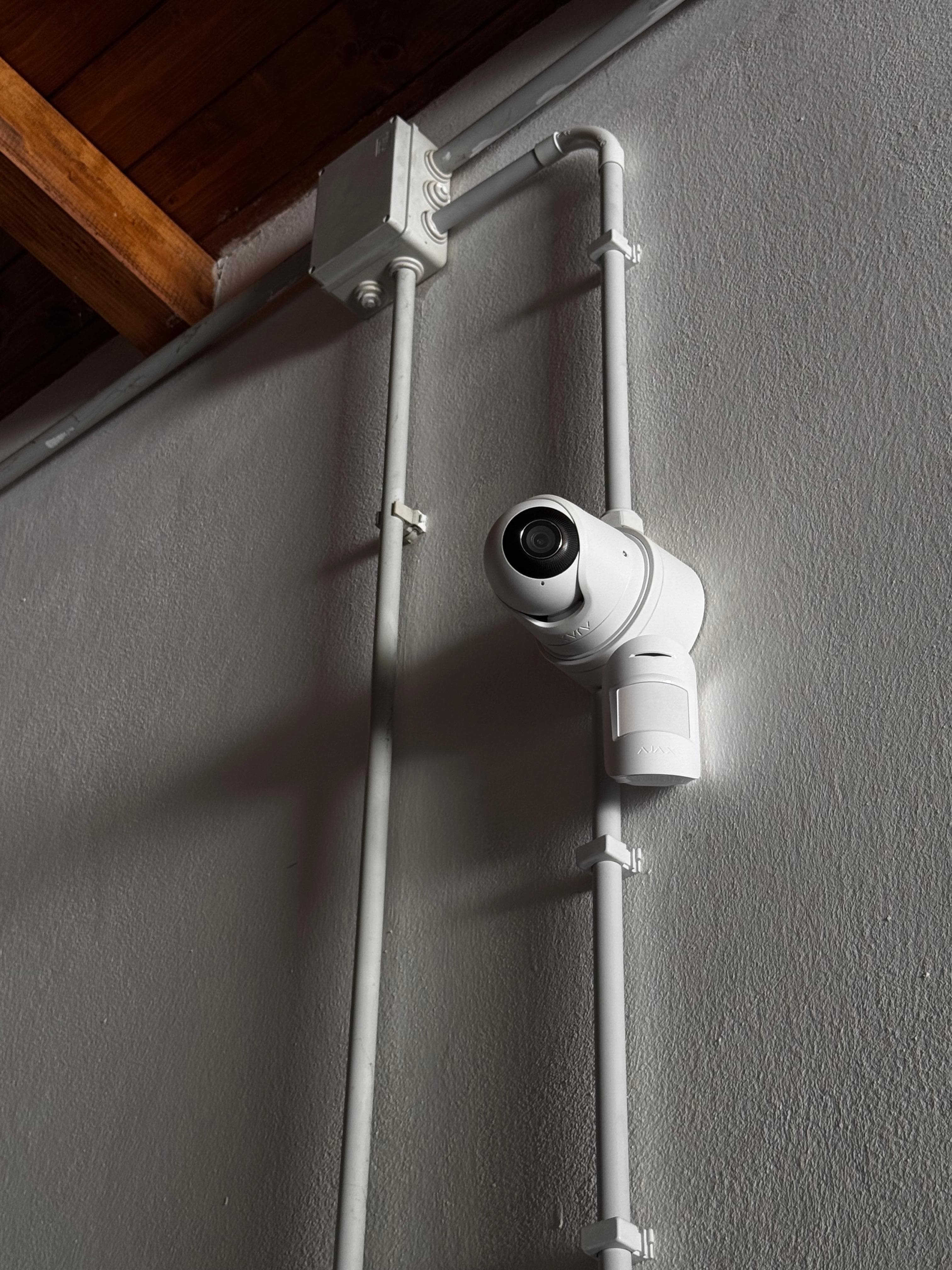 Telecamera di sicurezza bianca e sensore di movimento montati su parete con tubi protettivi.
